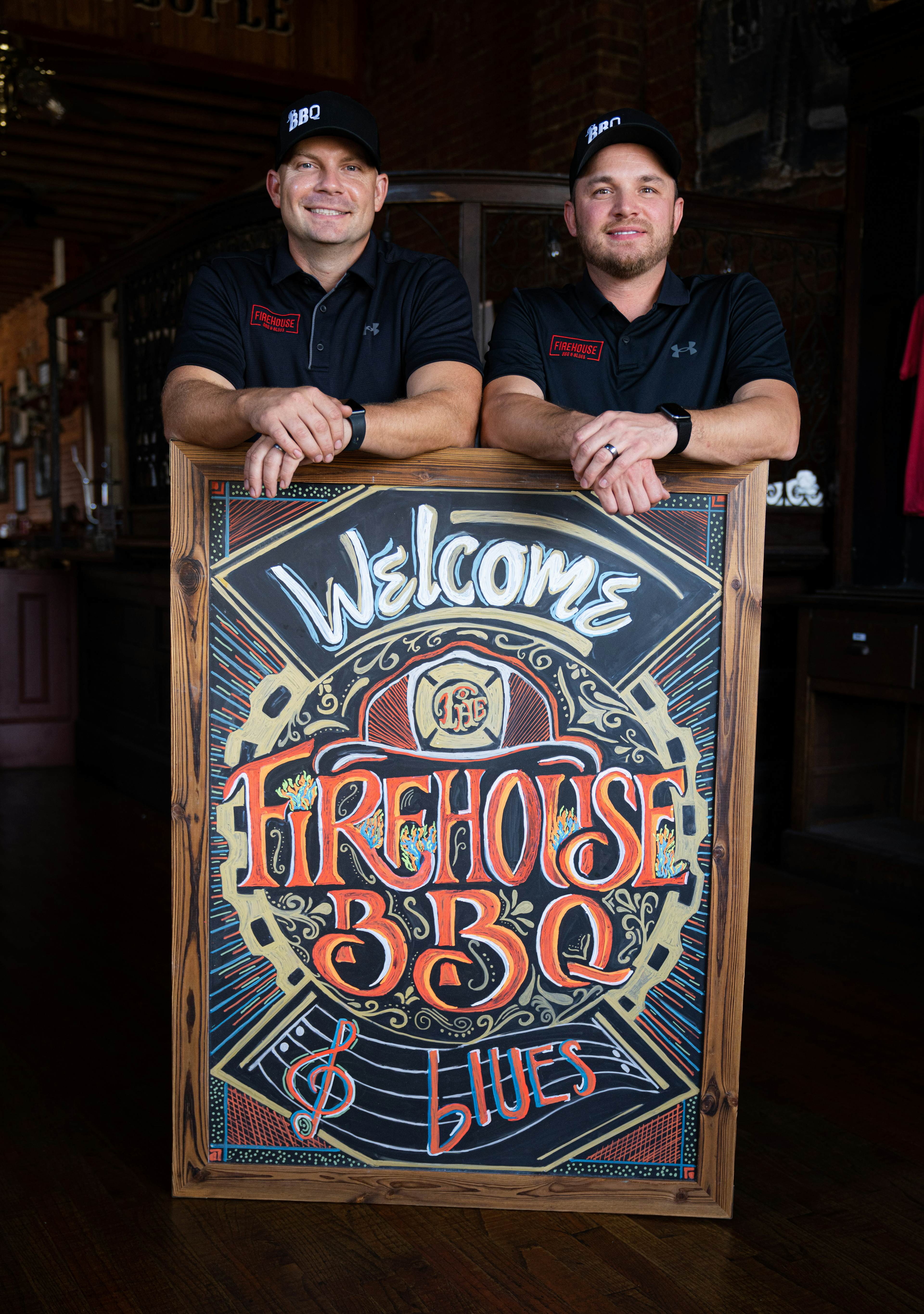 Nick Arbogast and Dustin Garvin standing behind the Firehouse BBQ & Blues welcome sign